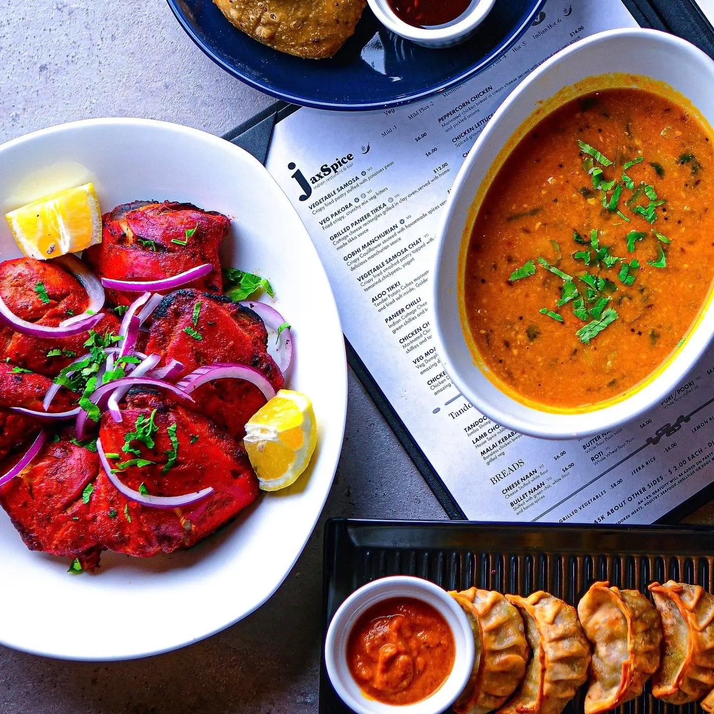 Overhead view of tandoori, a bowl of curry and momos on a JaxSpice menu